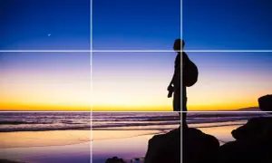 Sylwetka fotografa na plaży o zachodzie słońca, z księżycem na niebie. Kompozycja oparta na zasadzie trójpodział w fotografii.