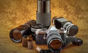 Kolekcja różnych rodzajów aparatów fotograficznych i akcesoriów: lustrzanka Pentax, obiektywy, mieszek, filmy.