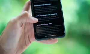 Dłoń trzyma smartfon, na ekranie którego widać opis formatu RAW. RAW to format pliku, który daje większą swobodę podczas obróbki zdjęć.
