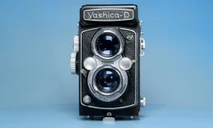 Czarno-srebrny aparat dwuobiektywowy Yashica-D na niebieskim tle.