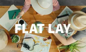 Widok z góry na stół z mapami, globusem, aparatem, notatnikiem i kawą. Dwie osoby planują podróż. To idealny flat lay.
