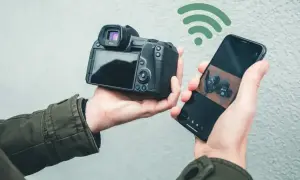 Dłoń trzyma aparat i smartfon połączone przez Wi-Fi. Aplikacja Canon Camera Connect pozwala na łatwe przesyłanie zdjęć.