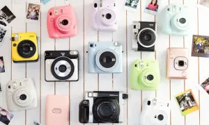 Kolekcja kolorowych aparatów Instax, co to za magia natychmiastowych zdjęć? Różowy, żółty, miętowy i inne, otoczone polaroidami.