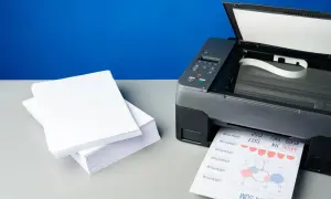 Stos białego papieru obok drukarki atramentowej, która właśnie drukuje dokument. Jaki papier do drukarki atramentowej wybrać, by uzyskać najlepsze rezultaty?
