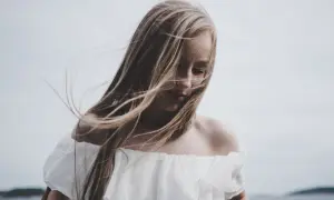 Dziewczyna z rozwianymi włosami w białej sukience. Kompozycja zamknięta podkreśla jej melancholijny nastrój.