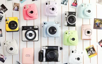 Kolekcja kolorowych aparatów Instax, co to za magia natychmiastowych zdjęć? Różowy, żółty, miętowy i inne, otoczone polaroidami.