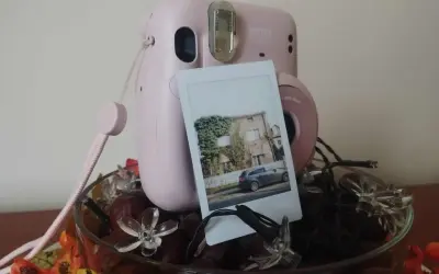 Różowy Instax Mini 11 z wywołanym zdjęciem domu i samochodu. Dowiedz się, jak robić zdjęcia Instax!