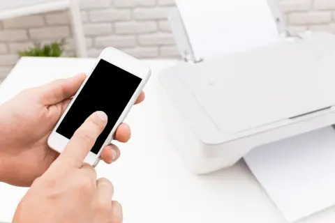Dłoń trzyma smartfon, obok drukarka HP. Prosty sposób, jak drukować z telefonu na drukarce HP przez WiFi.