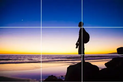 Sylwetka fotografa na plaży o zachodzie słońca, z księżycem na niebie. Kompozycja oparta na zasadzie trójpodział w fotografii.