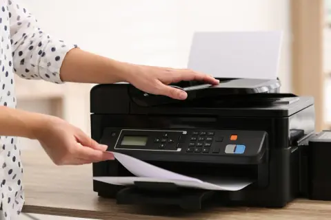 Ręce kładą papier na drukarce atramentowej czy laserowej, gotowe do drukowania.