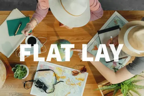 Widok z góry na stół z mapami, globusem, aparatem, notatnikiem i kawą. Dwie osoby planują podróż. To idealny flat lay.