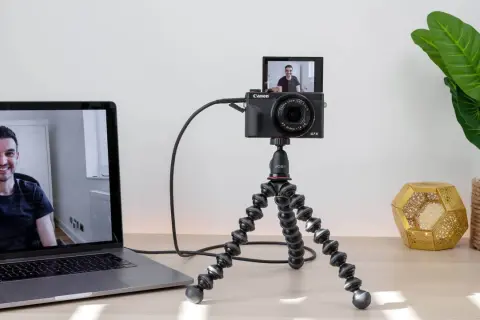 Ustawienie do streamingu: aparat Canon G7X na statywie Joby, podłączony do laptopa. Widoczny uśmiechnięty mężczyzna na ekranie. Idealne do streamingu z użyciem **EOS Utility**.