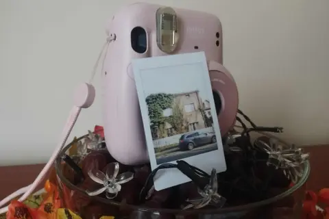 Różowy Instax Mini 11 z wywołanym zdjęciem domu i samochodu. Dowiedz się, jak robić zdjęcia Instax!