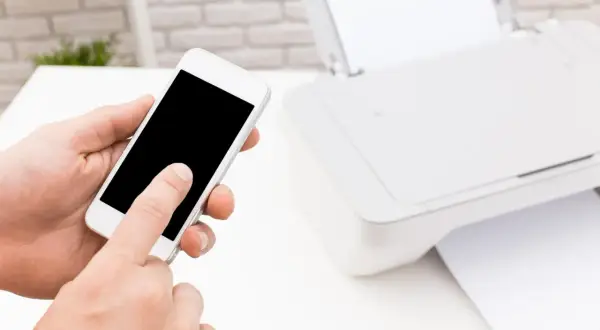 Dłoń trzyma smartfon, obok drukarka HP. Prosty sposób, jak drukować z telefonu na drukarce HP przez WiFi.