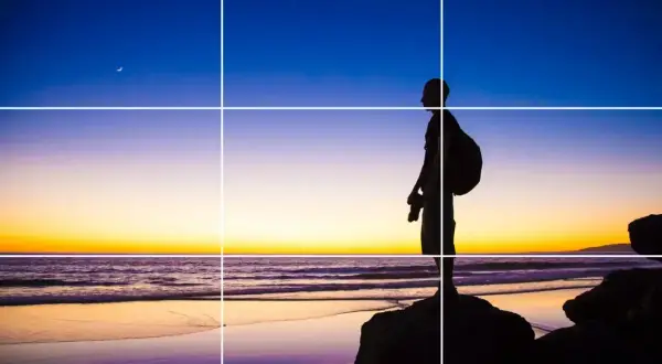 Sylwetka fotografa na plaży o zachodzie słońca, z księżycem na niebie. Kompozycja oparta na zasadzie trójpodział w fotografii.
