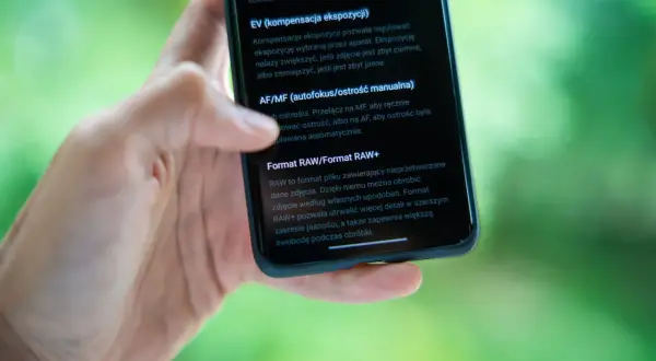 Dłoń trzyma smartfon, na ekranie którego widać opis formatu RAW. RAW to format pliku, który daje większą swobodę podczas obróbki zdjęć.