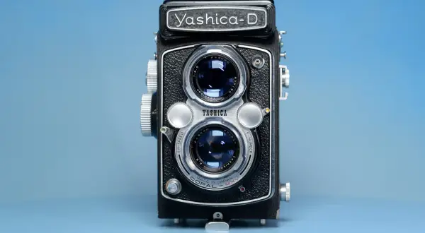 Czarno-srebrny aparat dwuobiektywowy Yashica-D na niebieskim tle.
