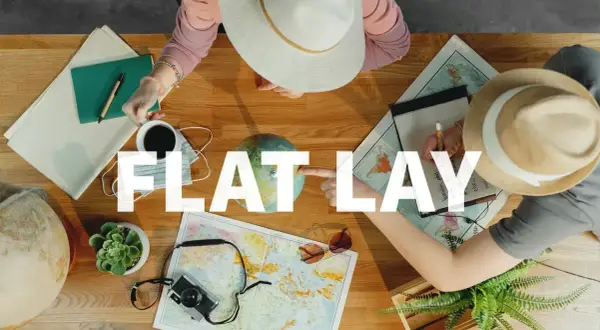 Widok z góry na stół z mapami, globusem, aparatem, notatnikiem i kawą. Dwie osoby planują podróż. To idealny flat lay.