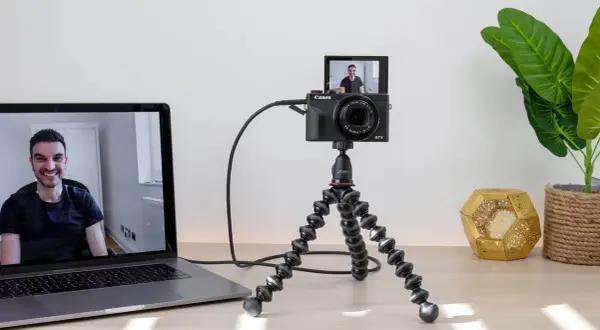 Ustawienie do streamingu: aparat Canon G7X na statywie Joby, podłączony do laptopa. Widoczny uśmiechnięty mężczyzna na ekranie. Idealne do streamingu z użyciem **EOS Utility**.