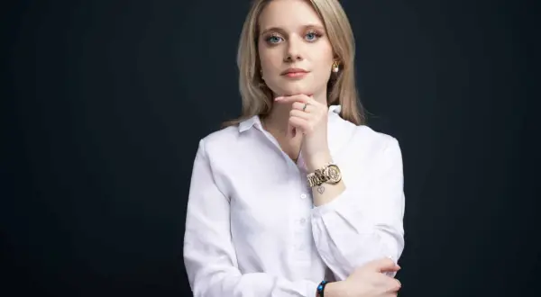Kobieta w białej koszuli, z ręką na podbródku, pokazuje, jak zrobić zdjęcie biznesowe w domu.