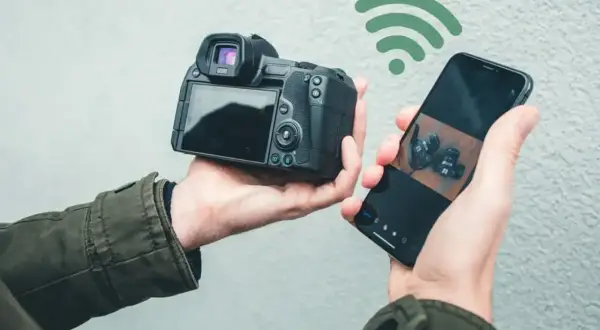 Dłoń trzyma aparat i smartfon połączone przez Wi-Fi. Aplikacja Canon Camera Connect pozwala na łatwe przesyłanie zdjęć.