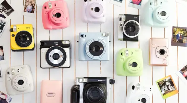 Kolekcja kolorowych aparatów Instax, co to za magia natychmiastowych zdjęć? Różowy, żółty, miętowy i inne, otoczone polaroidami.
