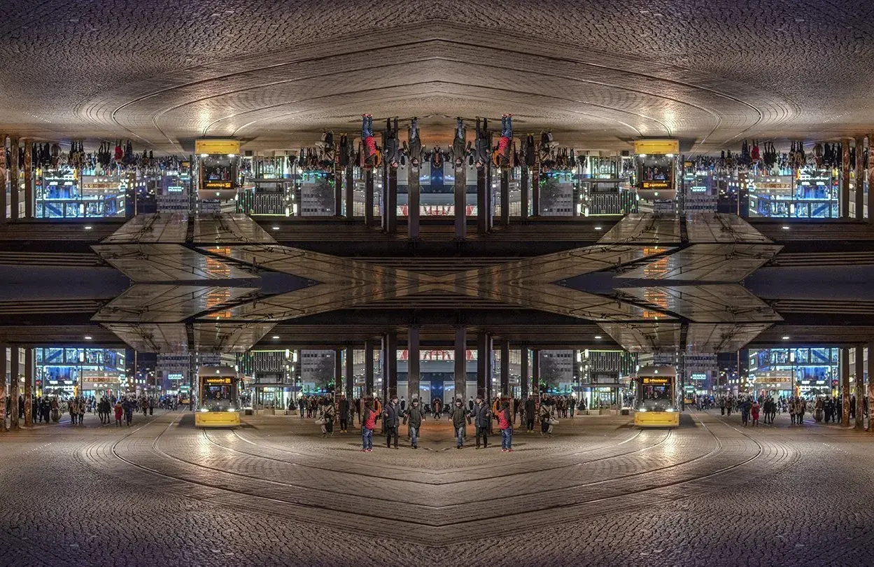 Nocne miasto z żółtym tramwajem i ludźmi, tworzące symetryczną, lustrzaną kompozycję.