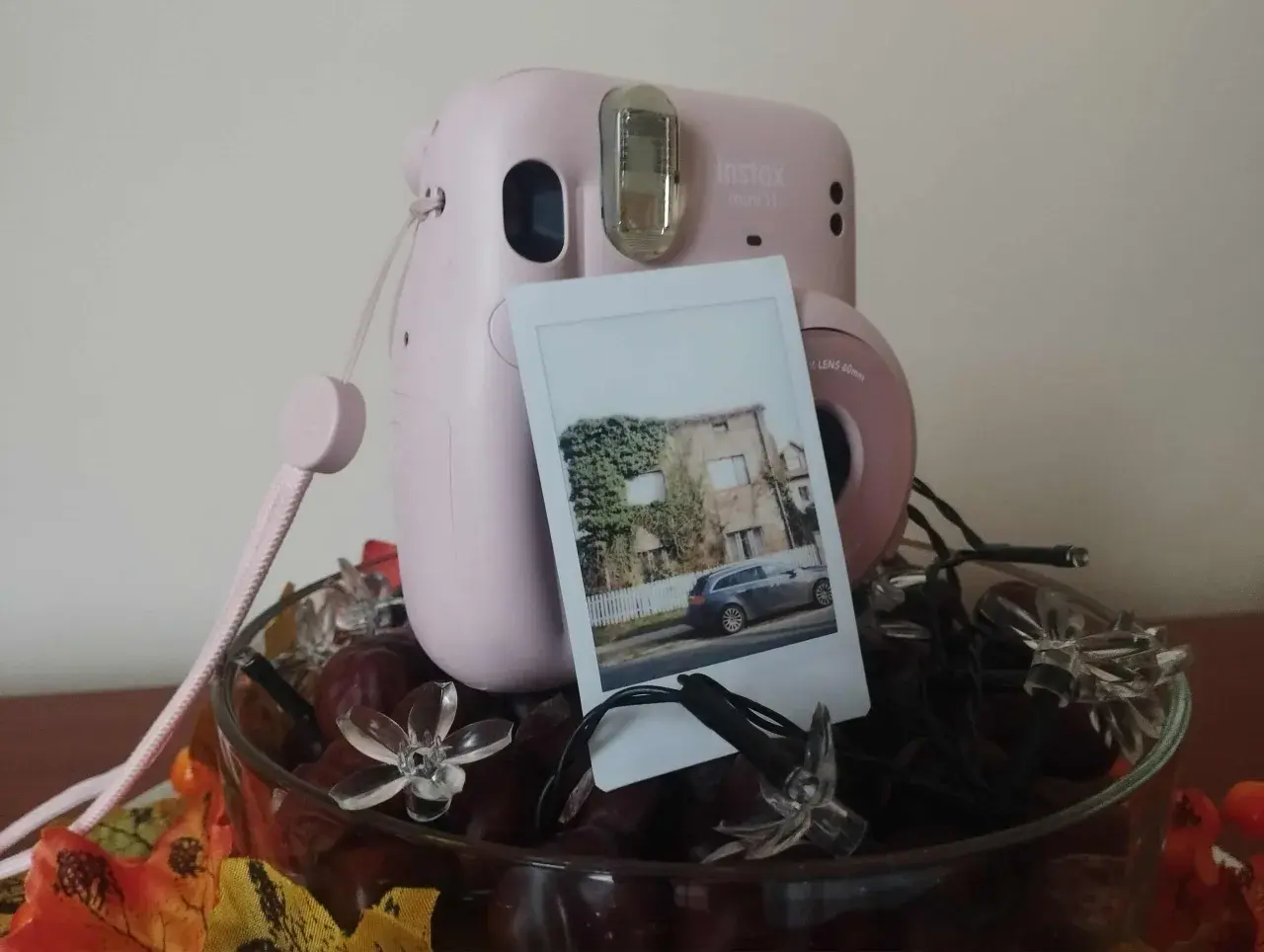 Różowy Instax Mini 11 z wywołanym zdjęciem domu i samochodu. Dowiedz się, jak robić zdjęcia Instax!