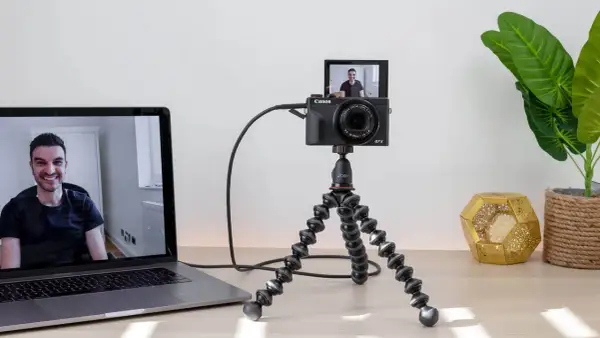 Ustawienie do streamingu: aparat Canon G7X na statywie Joby, podłączony do laptopa. Widoczny uśmiechnięty mężczyzna na ekranie. Idealne do streamingu z użyciem **EOS Utility**.