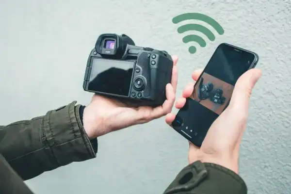 Dłoń trzyma aparat i smartfon połączone przez Wi-Fi. Aplikacja Canon Camera Connect pozwala na łatwe przesyłanie zdjęć.